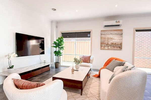 A modern living room with a flat-screen TV, comfortable seating, a coffee table, and a large window with a view.