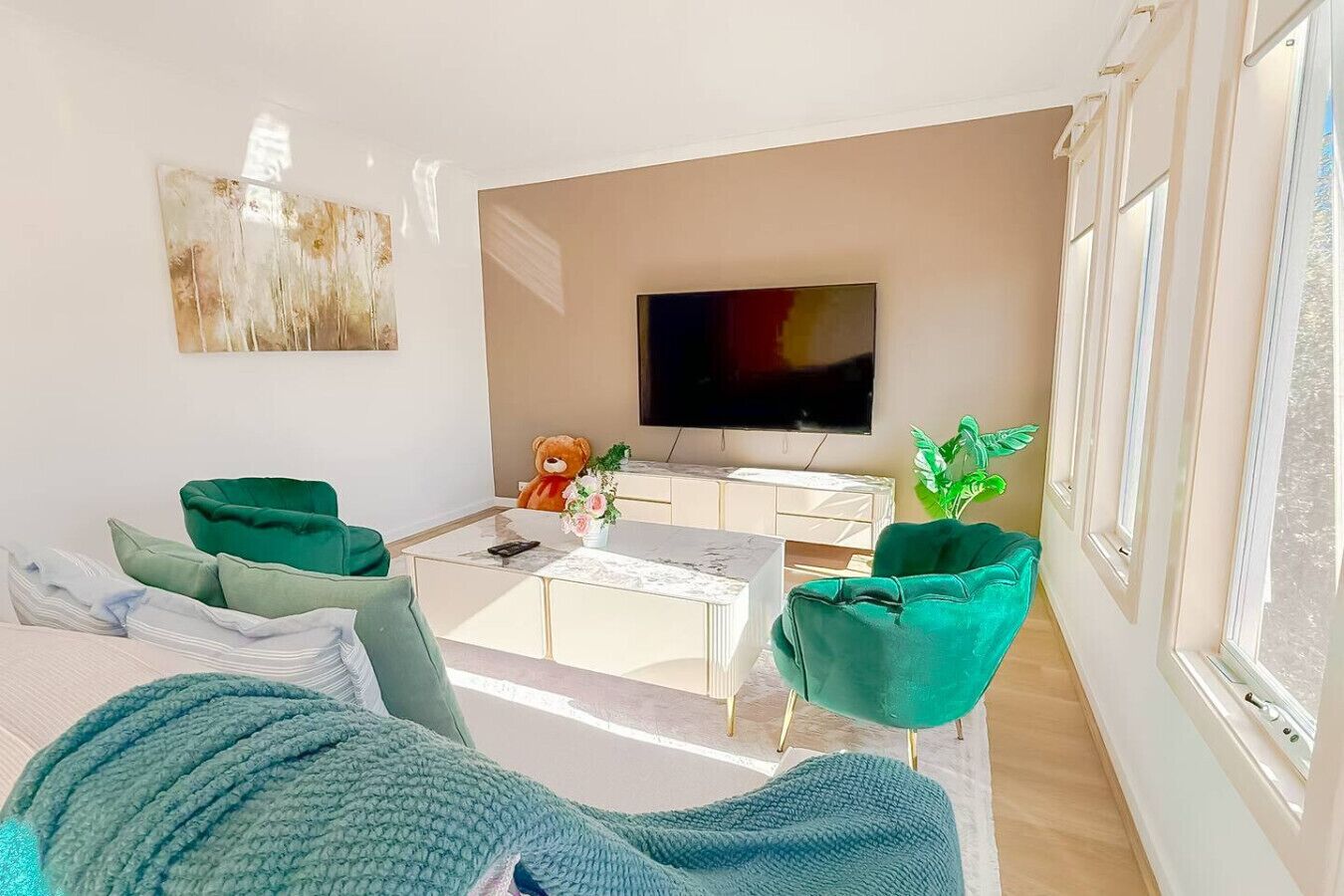A modern living room with a sofa, two green armchairs, a coffee table, a TV, a teddy bear, and a plant.
