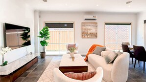 A spacious living room with a flat-screen TV, a comfortable sofa, a coffee table, and a dining area with chairs.