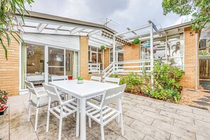Eine Terrasse mit weißem Tisch und Stühlen, eine Ziegelmauer und ein Gartenbereich mit Pflanzen.