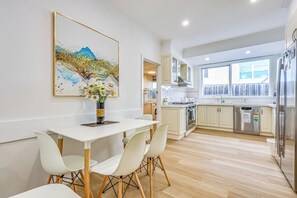 Eine moderne Küche mit weißen Schränken, einem Edelstahl-Kühlschrank und einem Essbereich mit weißem Tisch und Stühlen.