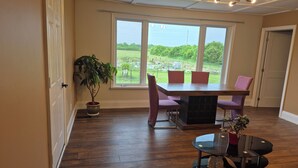 A dining area with a table and chairs, a potted plant, and a view of a green landscape through large windows. - Issa place (Prince Edward)