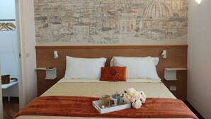 A hotel room with a large cityscape mural on the wall, a bed with white and orange pillows, a tray with toiletries, and a wooden headboard.