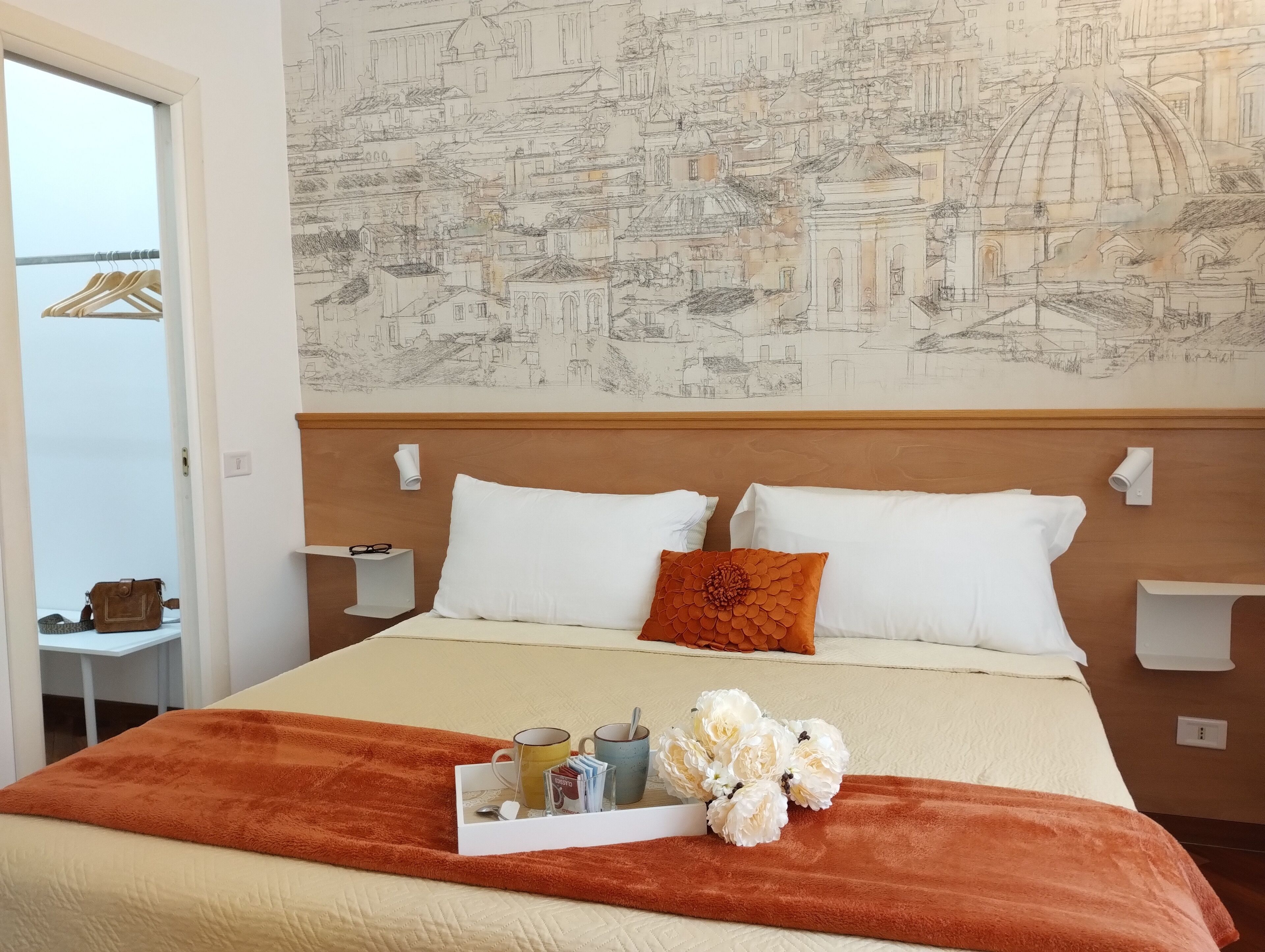 Een hotelkamer met een groot bed, een muurschildering van een stadsgezicht, een houten hoofdbord en een dienblad met toiletartikelen.