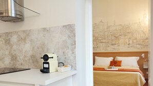 A modern hotel room with a minimalist design, featuring a white desk with a coffee maker, a small basket, and a wall with a cityscape mural.