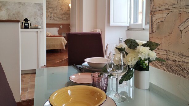 A hotel room with a dining area, a bed, a desk, and a large window.