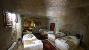 A room with four beds arranged in a U-shape, a radiator, a patterned rug, and a framed picture on the wall. - center cave house (Nevşehir)
