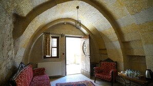 A room with a high arched stone ceiling, a red patterned sofa, a matching armchair, a wooden table with bottles, and a radiator. - center cave house (Nevşehir)