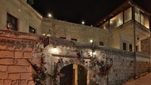 A stone archway with wooden doors, surrounded by climbing plants and flowers, leading to a building with a stone facade and a balcony. - center cave house (Nevşehir)