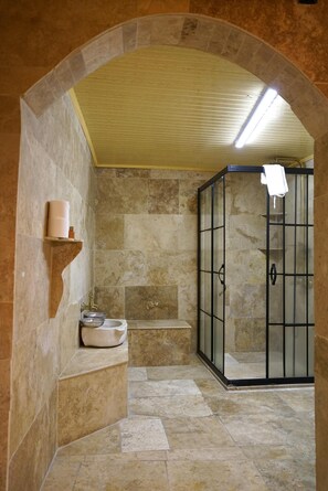 Une salle de bain aux murs en pierre, dotée d’une cabine de douche, d’un lavabo et d’une étagère où sont rangés les articles de toilette.