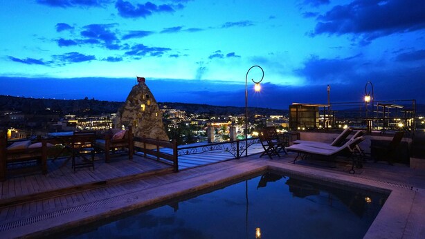 A rooftop pool area with lounge chairs and a stone structure, overlooking a cityscape at dusk. - center cave house (Nevşehir)
