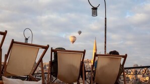 A rooftop terrace with wooden chairs and a view of the city skyline, including a prominent tower. - center cave house (Nevşehir)