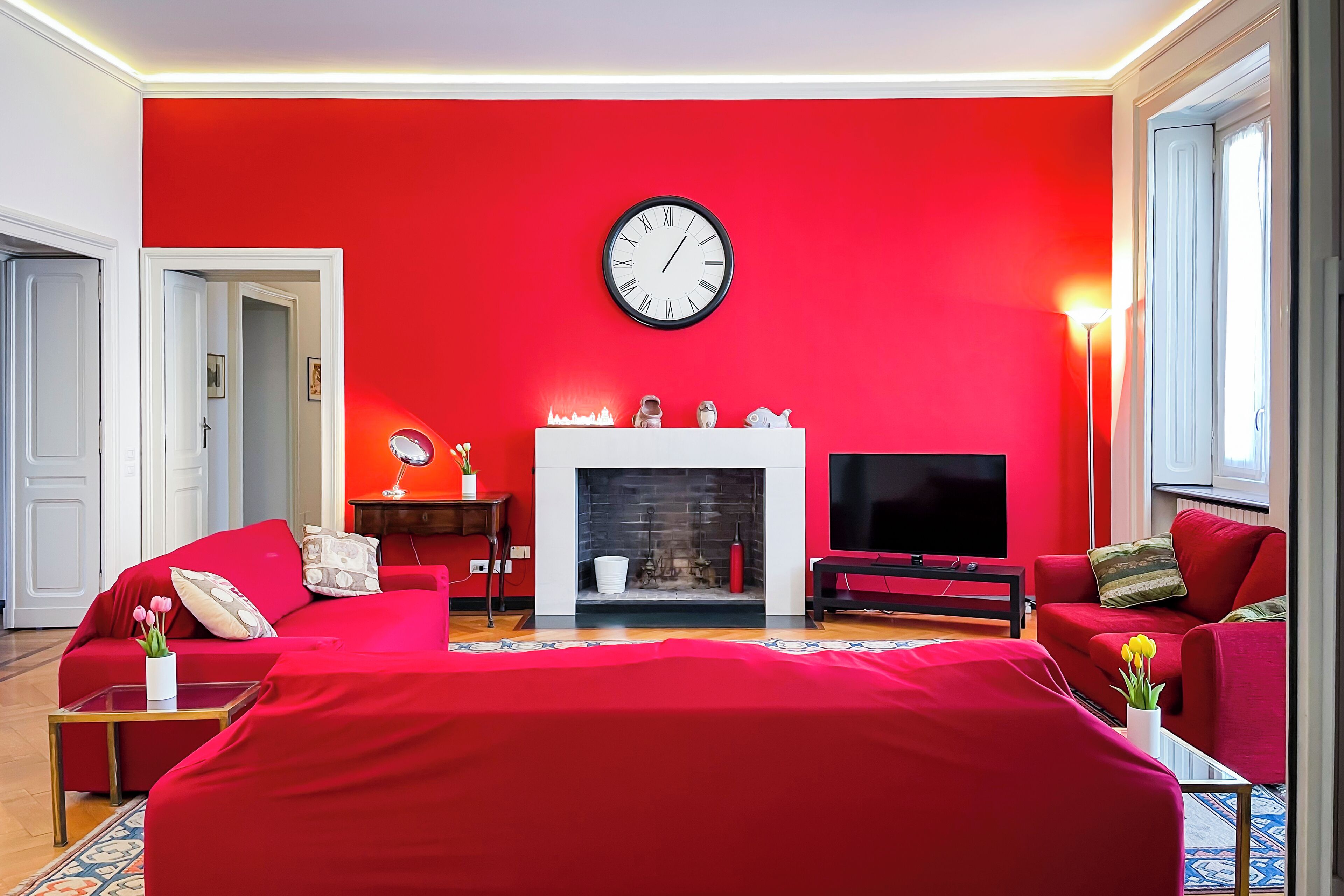 Un salon aux murs rouges, avec une cheminée, une horloge et des canapés rouges.