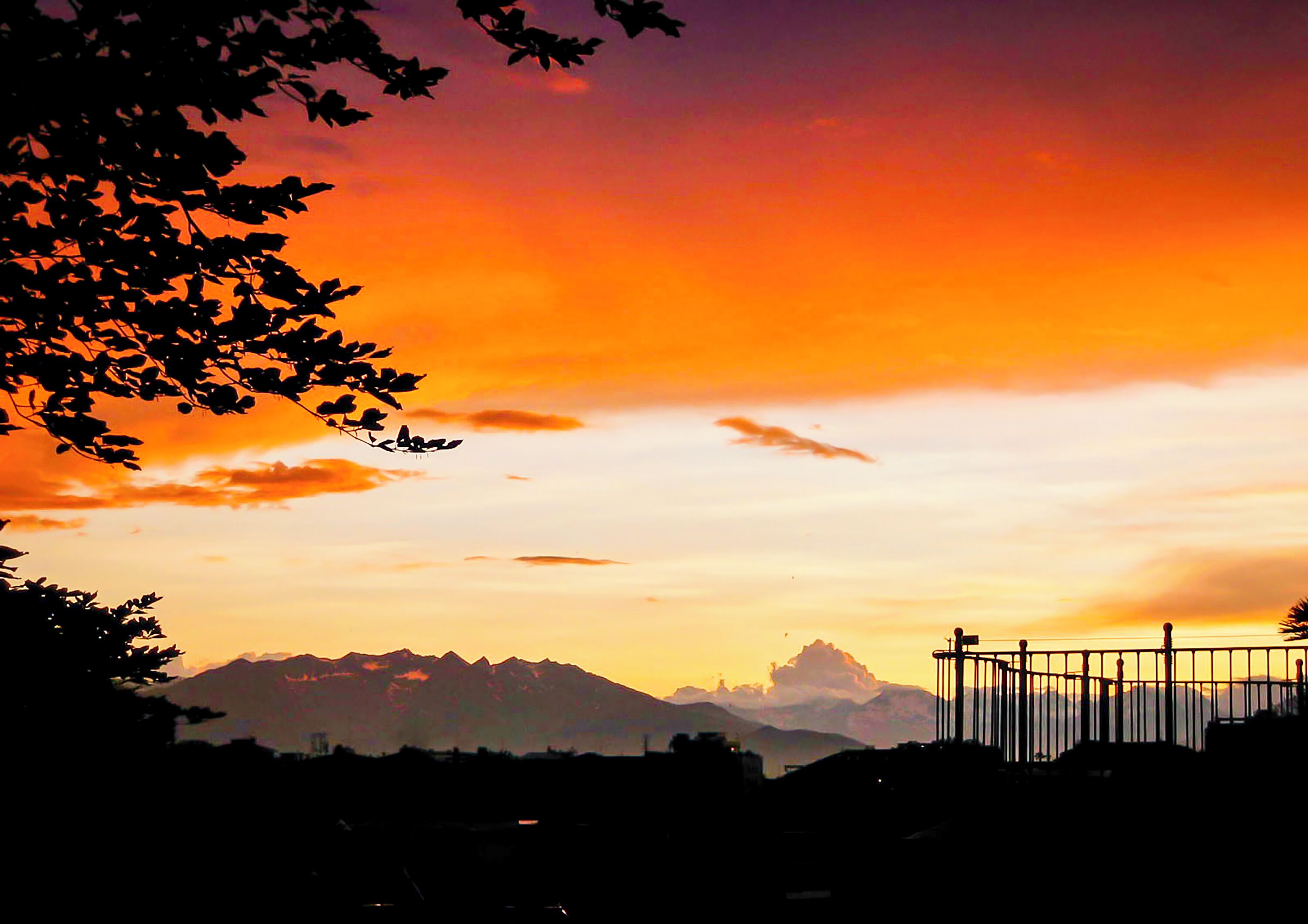 A sunset over mountains with a silhouette of a fence and trees.