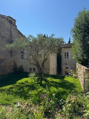 Un patio con muro de piedra, un árbol y un edificio con techo de tejas.