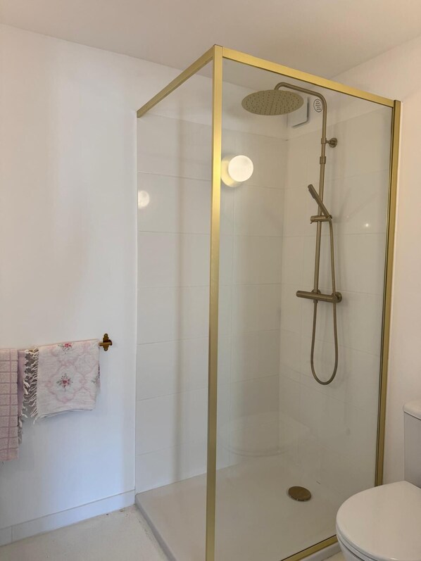 Un baño moderno con ducha envuelta en vidrio, inodoro blanco y toallero con una toalla estampada.
