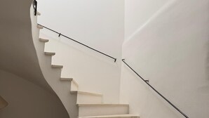 A white spiral staircase with a black handrail, leading to an upper floor.