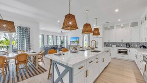Una cucina moderna con mobili bianchi, un'isola centrale e luci a sospensione.