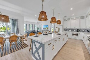 A modern kitchen with white cabinetry, a central island, and pendant lighting. - Amazing AMI House! Heated pool and hot tub! (Anna Maria)