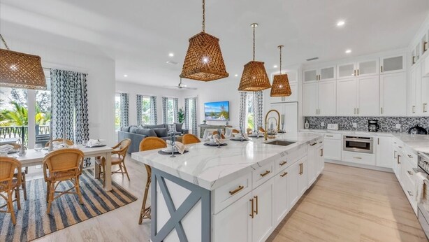 A modern kitchen with white cabinetry, a large island, and pendant lighting. - Amazing 6 bed house on Anna Maria! Putt putt, heated pool and spa! (Anna Maria)