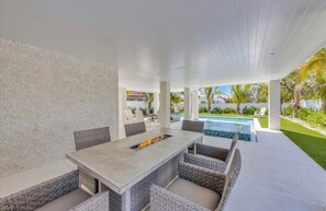Une terrasse extérieure avec une table et des chaises, un foyer et une vue sur une piscine.