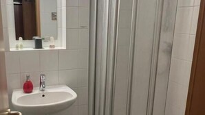 A bathroom with a white sink, a mirror, a shower enclosure, and a toilet. - Lachnerhof (Erlangen)