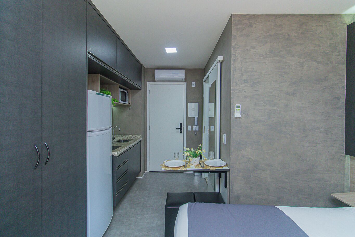 A compact hotel room with a kitchenette, a bed, and a small bathroom.