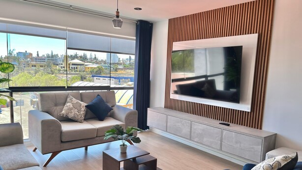 A modern living room with a large TV, a sofa, a coffee table, and a view of the city through large windows.