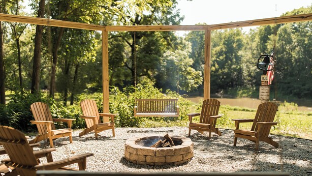 A covered outdoor seating area with Adirondack chairs, a fire pit, and a wooden bench. - The River House-- Secluded, Serene, Hot tub & Firepit (Bellbrook)