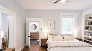 A bedroom with a large bed, bedside tables, a nightstand, a bookshelf, and a door leading to another room. - The River House-- Secluded, Serene, Hot tub & Firepit (Bellbrook)
