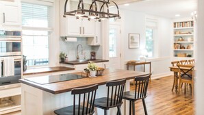 A modern kitchen with a central island, wooden chairs, and a hanging light fixture. - The River House-- Secluded, Serene, Hot tub & Firepit (Bellbrook)