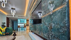 Un lobby moderno de hotel con un mostrador de recepción de mármol, un sofá verde y una zona de comedor con taburetes de bar.