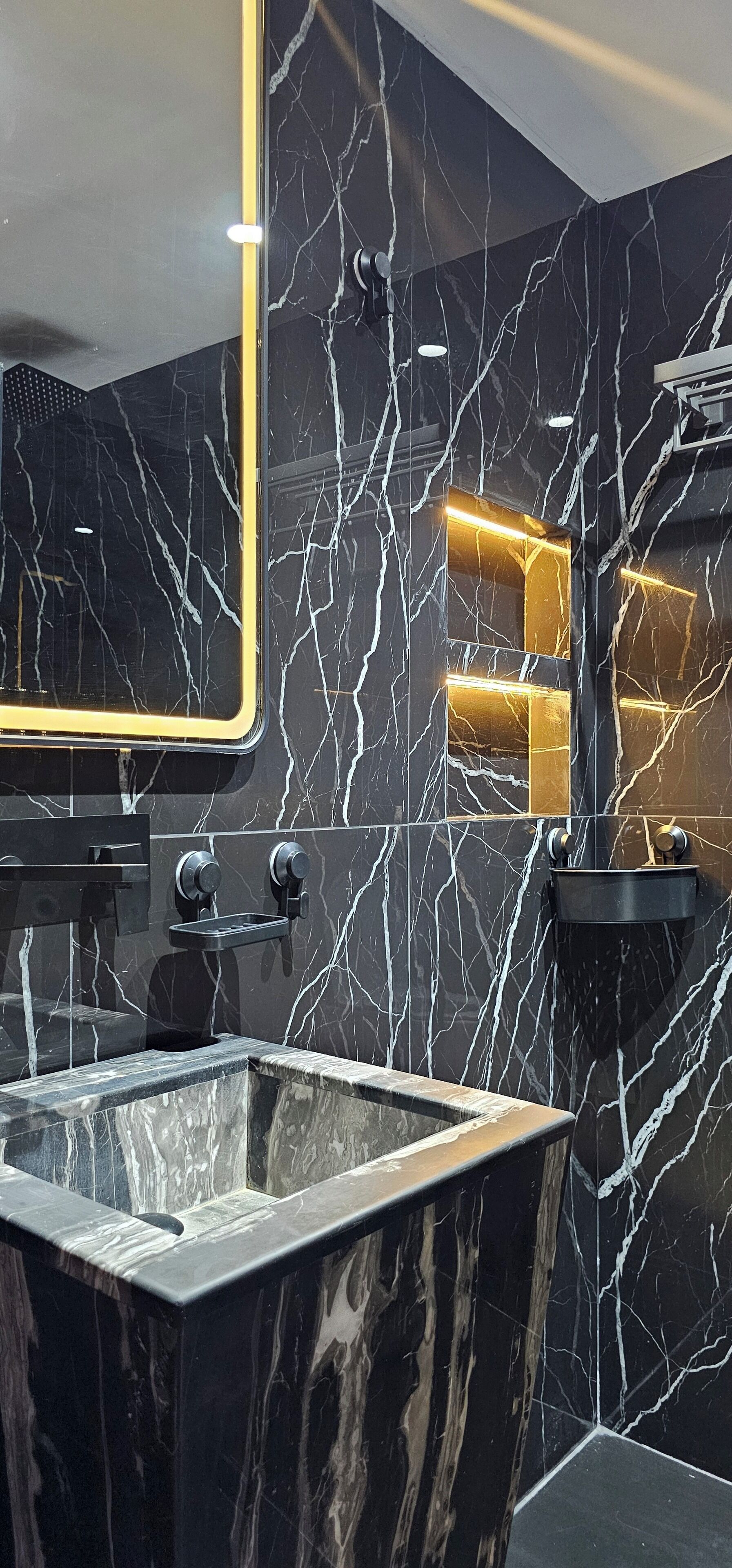 A modern bathroom with a black marble sink, gold fixtures, and a large mirror.