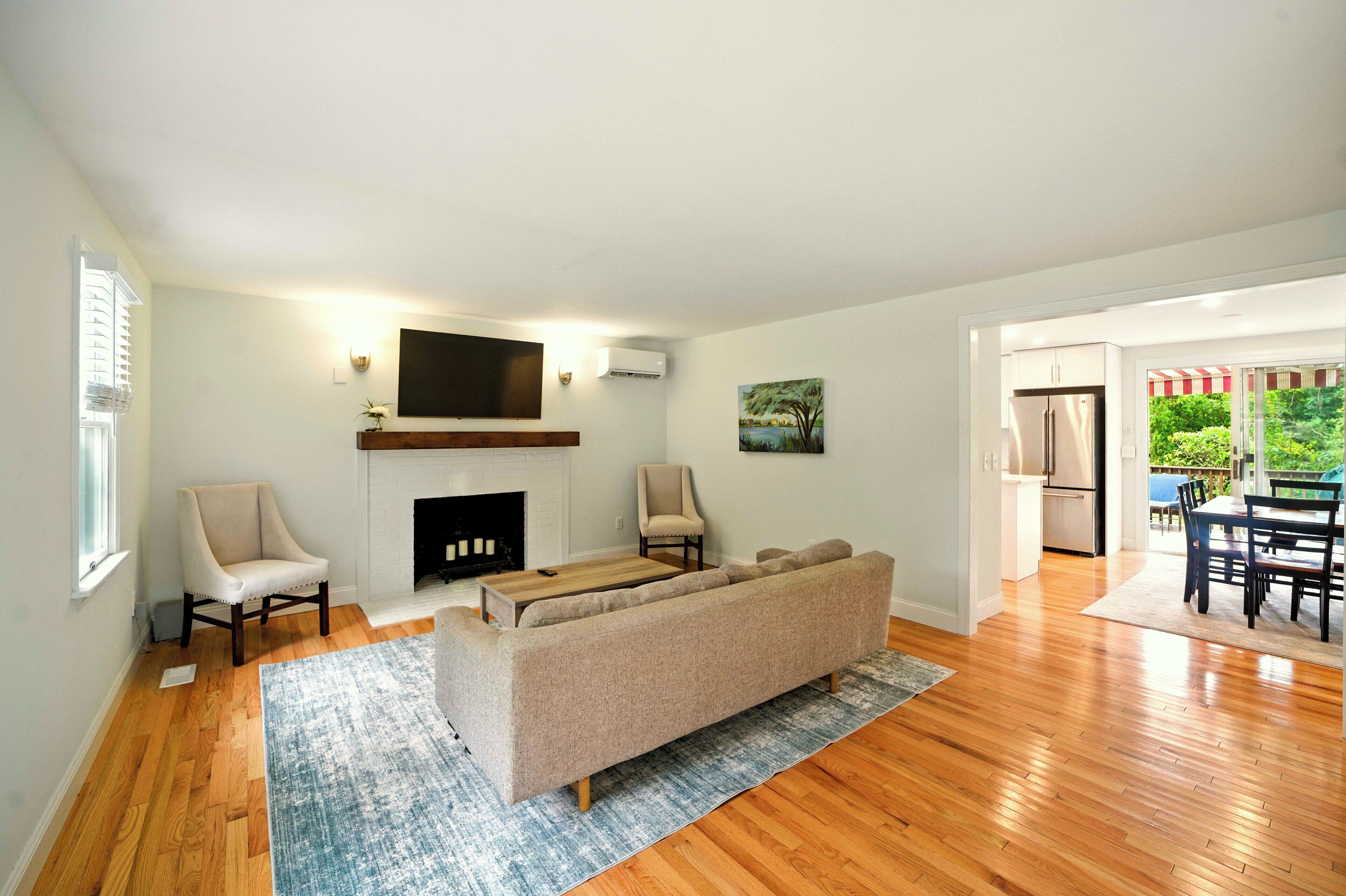 A living room with a fireplace, a sofa, two armchairs, a flat-screen TV, and a dining area with a table and chairs.