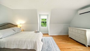 A bedroom with a bed, a dresser, a ceiling fan, and a window with a view of greenery.