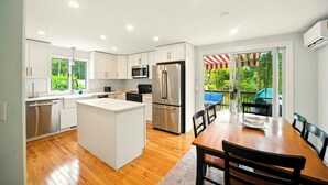 A modern kitchen with white cabinets, stainless steel appliances, and a wooden dining table.