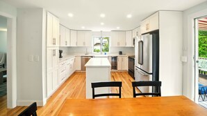 A modern kitchen with white cabinets, a central island, and a dining area with a wooden table and chairs.