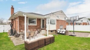 A brick house with a covered patio, outdoor seating, and a basketball hoop. - Spacious 5BR Home Private Backyard Basket Ball Hoop Near NY& Long Island Beaches (Syosset)