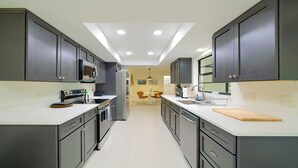 Een moderne keuken met donkere kastjes, witte aanrechtbladen en een centraal kookeiland. Er is een magnetron, oven en spoelbak.
