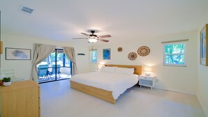 Een slaapkamer met een groot bed, een plafondventilator, een nachtkastje en uitzicht op een tuin via een schuifdeur.