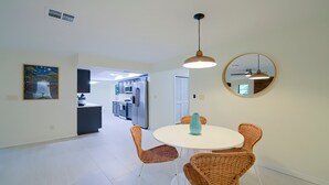 Een moderne keuken met roestvrijstalen apparatuur, een eethoek met rieten stoelen en een ronde spiegel aan de muur.
