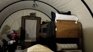 A tented room with bunk beds, a wooden dresser, and a door with a sign.