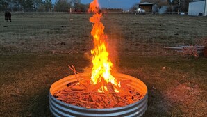 A metal fire pit with burning wood in an open field.