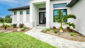 A modern house with a stone pathway leading to the entrance, surrounded by various plants and a well-maintained lawn. - VILLA BRILLANTE, A BRAND NEW Luxury Waterfront home  Pool/Spa & Gulf Access (Cape Coral)