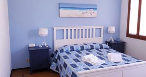 A bedroom with a bed, two nightstands, a painting, and a window.