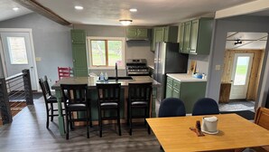 A modern kitchen with green cabinets, a wooden dining table, and a large window. - Rogers Creekside Ranch - Wessington Springs, SD - 3+ Bed, 1 Bath (Wessington Springs)