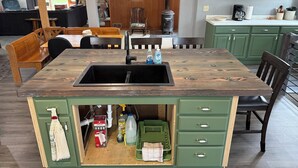 A kitchen with a wooden island sink, green cabinets, and a dining area with chairs and a table. - Rogers Creekside Ranch - Wessington Springs, SD - 3+ Bed, 1 Bath (Wessington Springs)
