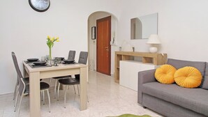 Un soggiorno moderno con un divano grigio, un tavolo da pranzo con quattro sedie e un piccolo tavolino con una lampada.