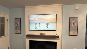 A living room with a fireplace, a mounted TV, and framed artwork on the walls. - Dockside Dreamz- Full duplex lake fun for 12 (Clarksville)