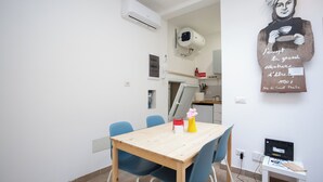 A dining area with a wooden table and blue chairs, a small white table with a computer and a cutting board, and a wall-mounted air conditioner. - Luminous apartment with private terrace in the colosseum (Roma)